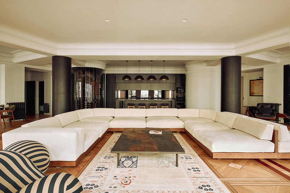 Salón abierto con sofá curvo y columnas negras en vivienda diseñada por Muka Arquitectura